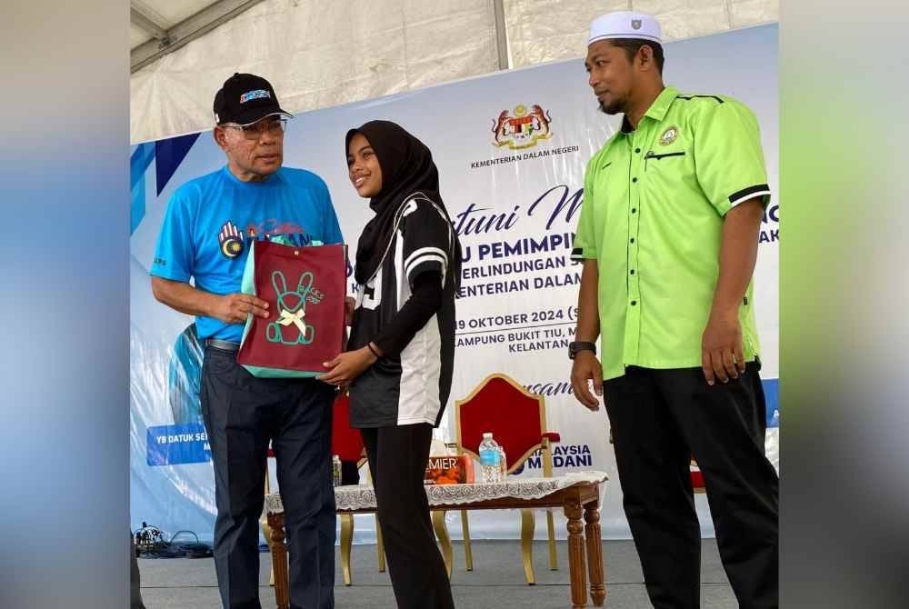 Saifuddin Nasution (kiri) menyampaikan sumbangan kelangkapan sekolah kepada penerima semasa Santuni Madani, Program Satu Pemimpin Satu Kampung Agensi Kawalan dan Perlindungan Sempadan Malaysia (MCBA) KDN di Kampung Bukit Tiu, Machang pada Sabtu.