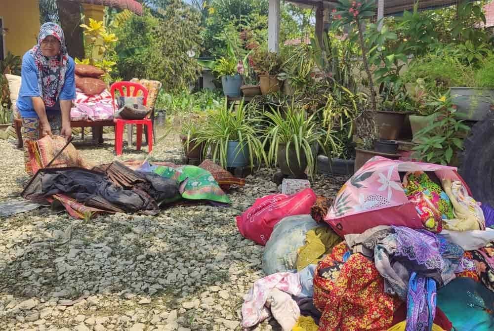Khatijah mengalihkan pakaian dan barangan selepas rumahnya ditenggelami banjir.