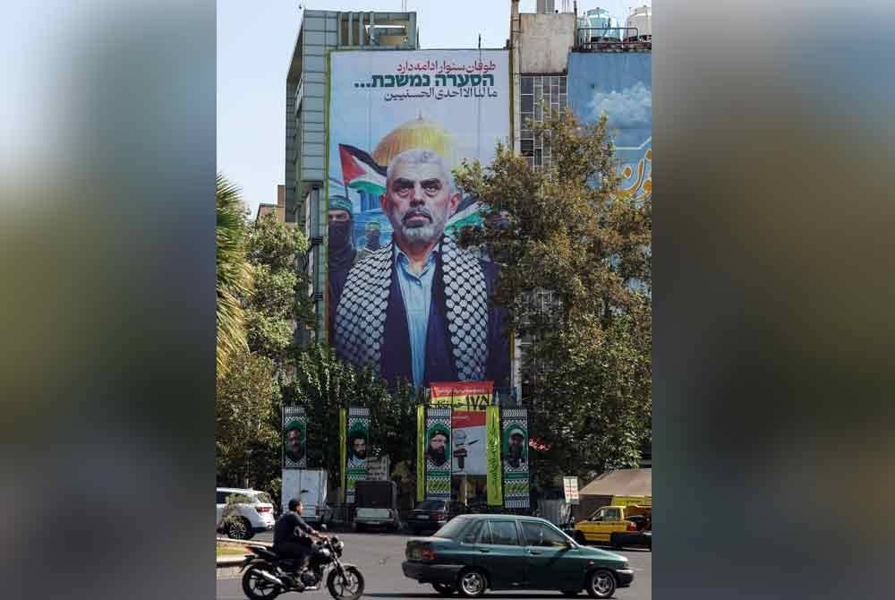 Orang ramai memandu melepasi papan iklan gergasi yang memaparkan wajah Yahya Sinwar yang dipasang di dataran Palestin di Teheran, Iran.