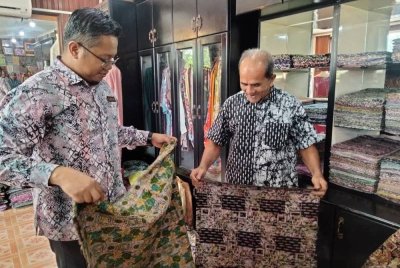 Mohd Hafiz (kiri) menunjukkan batik yang disiapkan di bengkelnya.