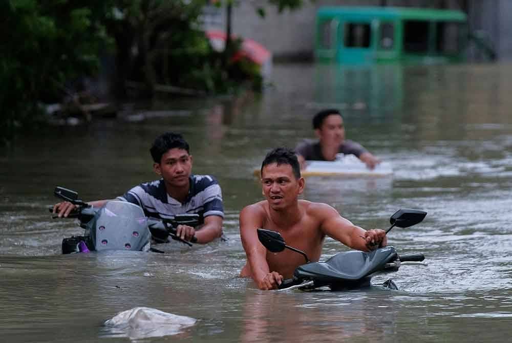 Penduduk menolak motosikal mereka meredah banjir di bandar Naga, wilayah Camarines Sur.