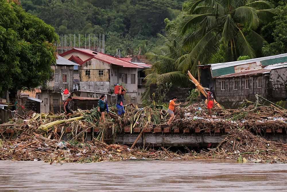 Penduduk menyeberangi jambatan yang dipenuhi longgokan sampah dibawa oleh Trami di bandar Polangui, wilayah Albay.
