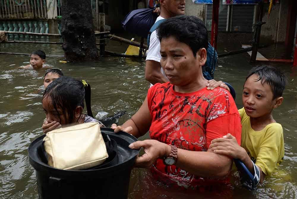 Seorang wanita bersama anak-anaknya mengharungi jalan yang dinaiki air di bandar Calumpit, wilayah Bulacan.