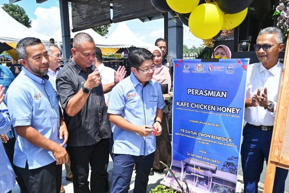 Ewon(tiga dari kiri) ketika menyempurnakan simbolik pelancaran kafe itu sambil diperhatikan oleh Suris(kanan)