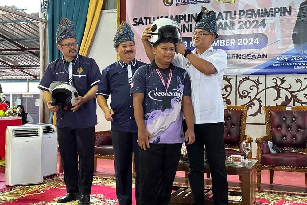 Makhzan (kanan) memakaikan topi keledar kepada penerima sambil diperhatikan Muhammad Kifli (dua dari kiri) ketika Program Satu Kampung, Satu Pemimpin, Santuni Madani 2024 di SMK Bukit Jawa pada Ahad.
