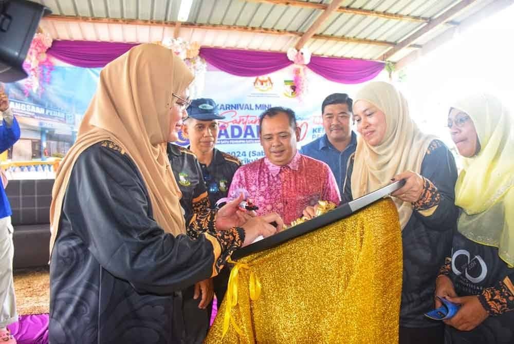 Noridah menandatangani plak Jubli Berlian sempena sambutan 100 tahun SK Pedah sambil diperhatikan Guru Besar sekolah, Azman Ismail (tengah).