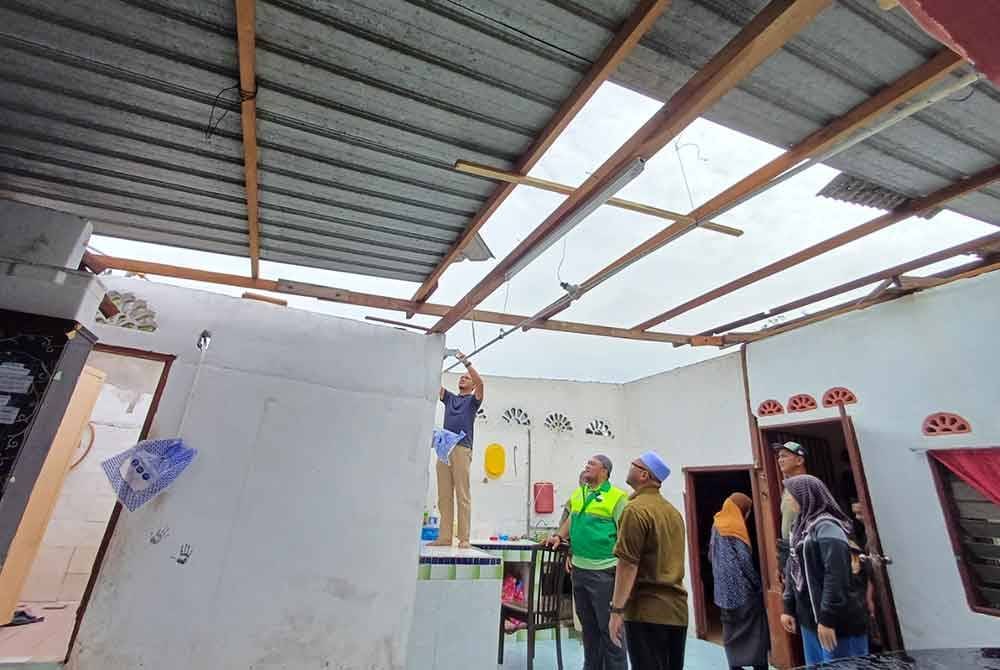 Mohd Tarmizi (tengah) melihat keadaan rumah Norsalizai yang rosak akibat ribut.