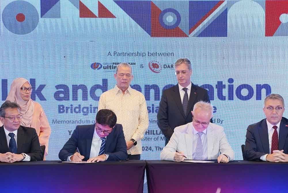 Azizi (dua dari kiri) menandatangani memorandum perjanjian persefahaman dengan Ketua Pengarah Darphane, Abdullah Yasir Sahin (dua dari kanan) disaksikan oleh Fadillah (berdiri, dua dari kiri) pada majlis Menandatangani Perjanjian Persefahaman antara Ultimate Print Sdn. Bhd dan Darphane pada Khamis.