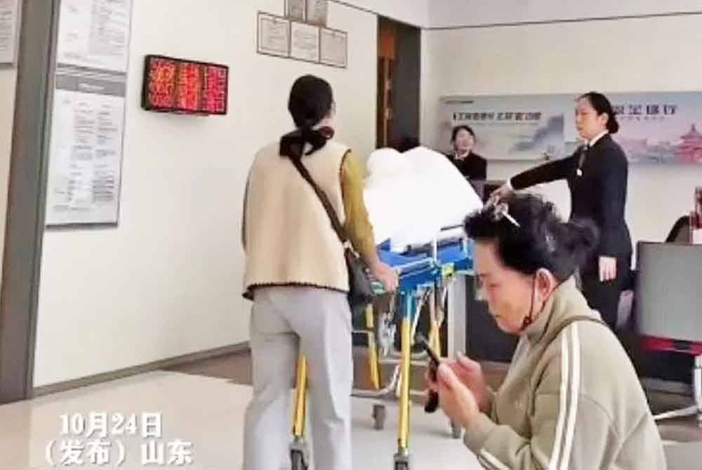 Keluarga lelaki ini hadir ke bank dengan menggunakan katil hospital untuk pengesahan identiti bagi pengeluaran wang. - Agensi