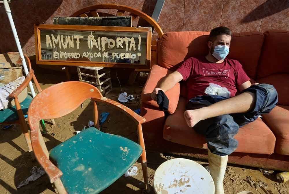 Seorang lelaki berehat bersebelahan serpihan perabot yang dihanyutka air banjir di Paiporta.