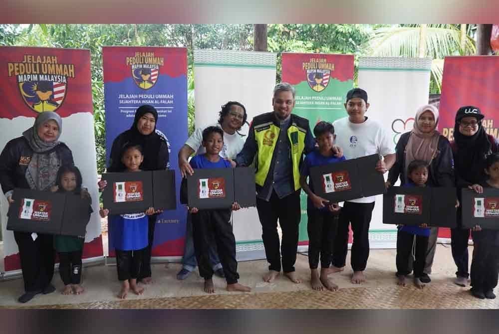 Setiausaha Agung Mapim, Muhammad Faris Hussien (lima dari kanan) menyerahkan sumbangan kepada penduduk Orang Asli.