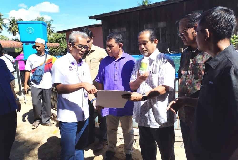 Ahmad Ramzi (kiri) melihat pelan pembangunan projek sempena program pelepasan anak ikan tilapia di Kampung Gong Mak Som di Besut.