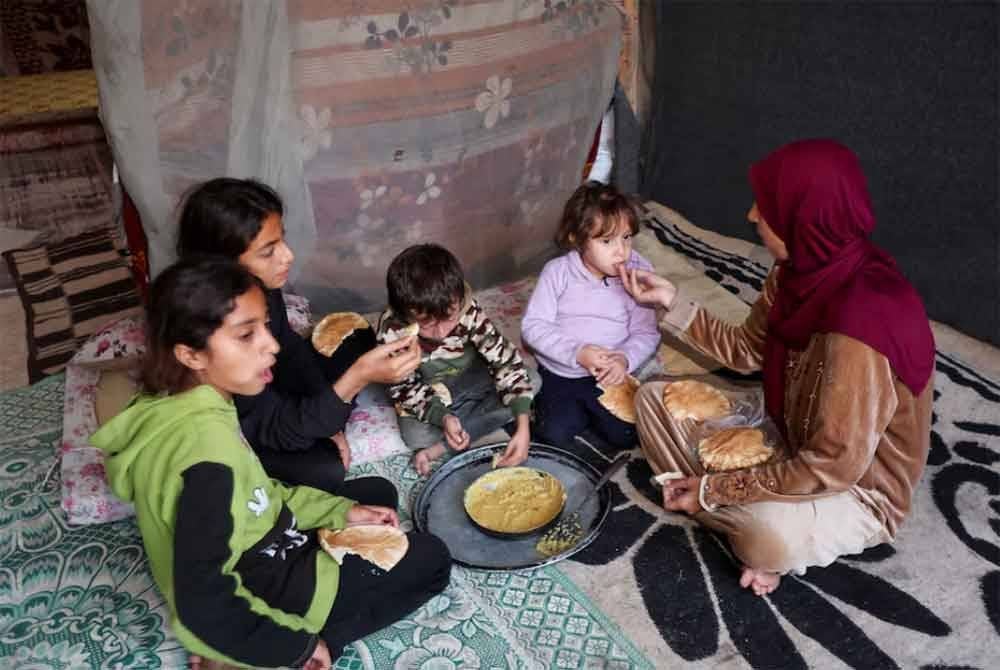 Qanou menyuap roti kepada anak-anaknya.