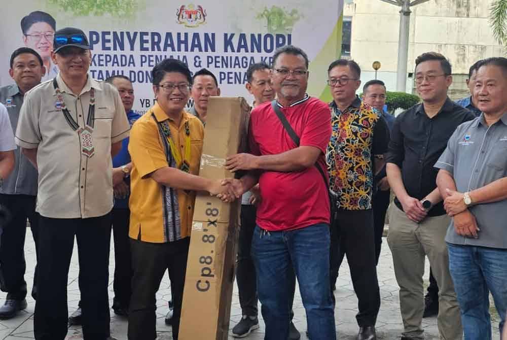 Ewon (dua dari kiri) menyampaikan kanopi kepada salah seorang peniaga di Tamu Donggongon, Penampang.