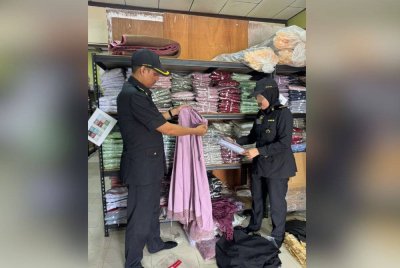 Anggota KPDN memeriksa telekung yang disyaki menggunakan jenama tiruan di Rengit, Batu Pahat.