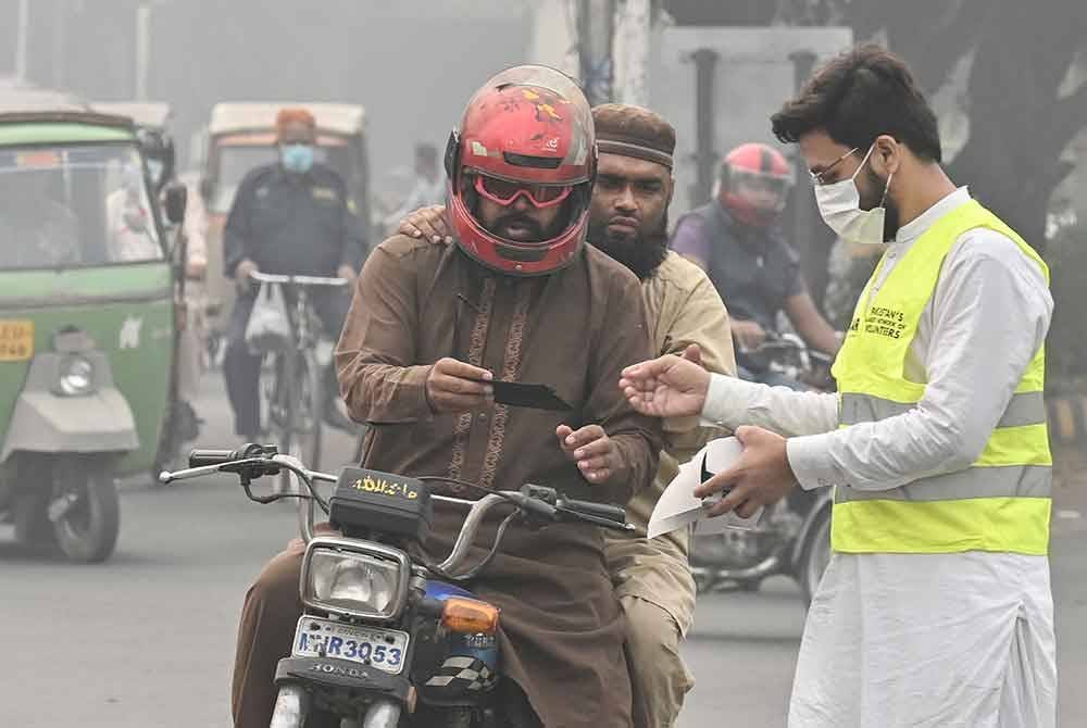 Sukarelawan awam Pakistan mengedarkan pelitup muka kepada orang ramai yang melalui jalan raya di Lahore.