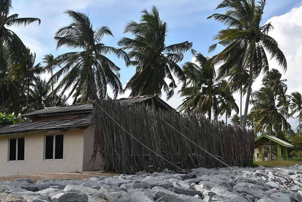 Penduduk memasang pelepah kelapa di pekarangan rumah sebagai benteng bagi menghalang angin kencang mengenai rumah ketika tinjauan FotoBernama di Pantai Damat hari ini.