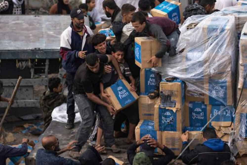Penduduk Palestin yang kelaparan menyerbu trak bantuan selepas ia melintasi sempadan Rafah ke Gaza pada Disember 2023. - Foto Agensi