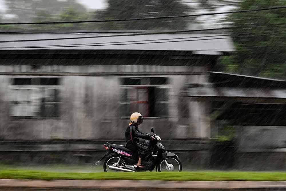 Penunggang motosikal meredah hujan di Bukit Payong dekat Marang hari ini.