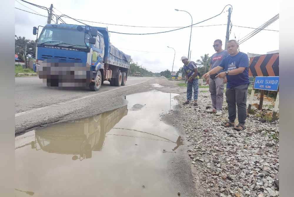 Mohd Fahmizan (kanan) menunjukkan Jalan Iskandar yang mengalami kerosakan teruk akibat sering digunakan kenderaan berat.