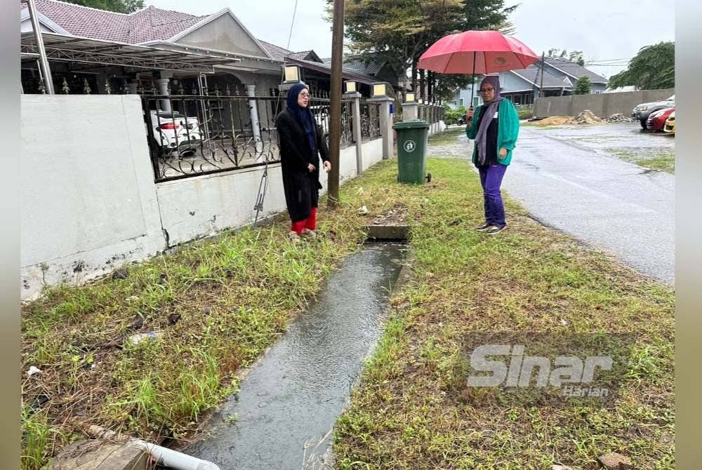 Ida Ruhayu (kiri) dan Asmah (kanan) melihat parit bersaiz kecil yang menjadi laluan air. Foto Sinar Harian ADILA SHARINNI WAHID