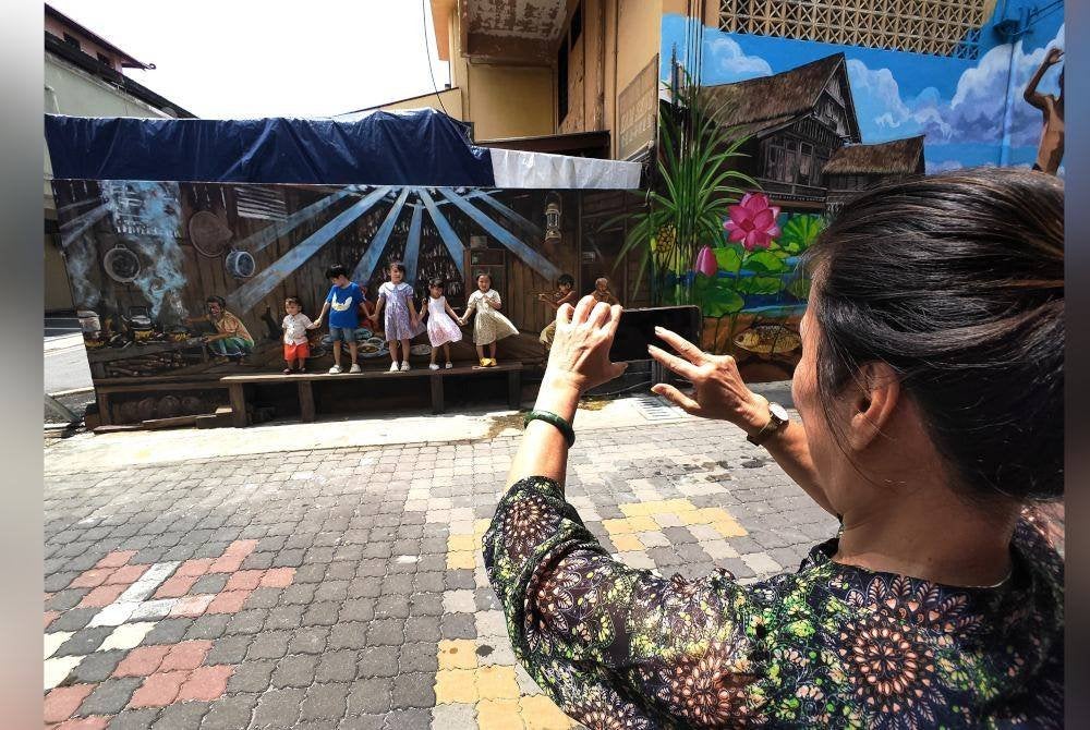 Seorang wanita mengambil gambar cucu-cucunya yang berdiri berlatarbelakangkan lukisan mural.