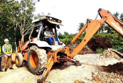 Manndzri (kanan) melakukan gimik perasmian dengan mengendalikan jengkaut pada Majlis Perasmian Pecah Tanah Depo Skrap di Kampung Paya Burma pada Sabtu.