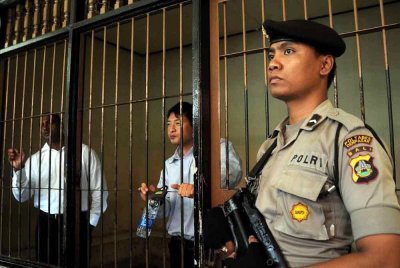 Seorang anggota polis berkawal di sebelah bilik tahanan di mana warga Australia Myuran Sukumaran (kiri) dan Andrew Chan (tengah), ahli kumpulan Bali Nine, menunggu perbicaraan mereka di Denpasar, Bali pada 8 Oktober 2010. - Foto: AFP