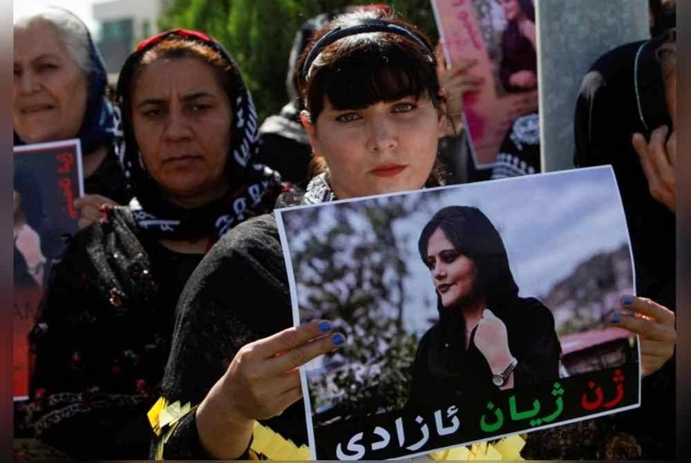 Seorang wanita memegang poster Mahsa Amini semasa mengadakan tunjuk perasaan di ibu pejabat PBB di Erbil, Iraq. - Agensi