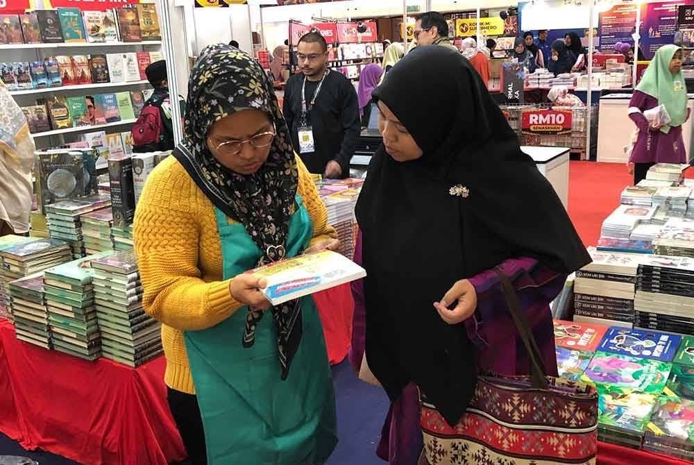 Staf menerangkan kepada pengunjung mengenai buku yang dijual.