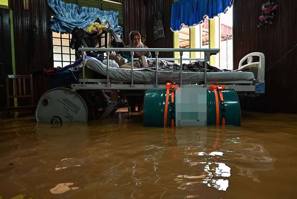 Usaha Zulkifli membuahkan hasil apabila katil yang telah diikat bersama tiga tong dram besi berjaya diapungkan meskipun air naik ke dalam rumahnya sehingga ke paras paha pada tengah hari Rabu lepas. - Foto: Bernama
