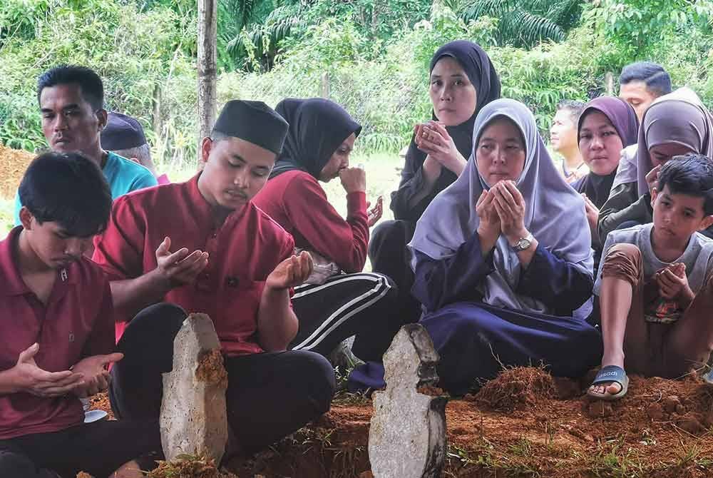 Ruziah (dua dari kanan) berdoa selepas jenazah dua anaknya dikebumikan di Tanah Perkuburan Kampung Panggong di Ajil, Hulu Terengganu pada Sabtu.