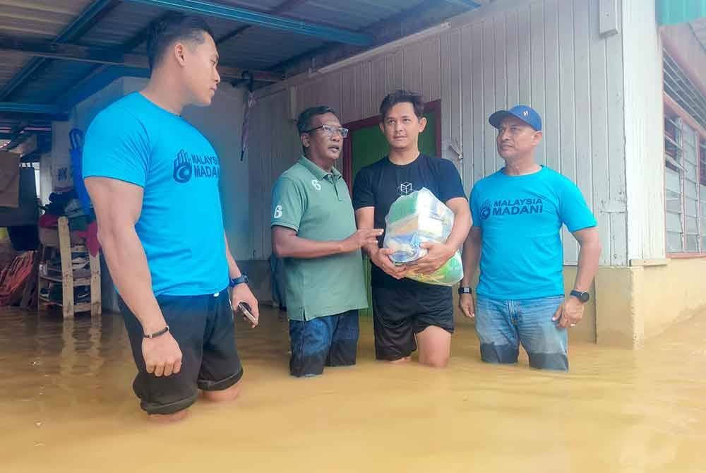 Zuraidi (dua kiri) menyampaikan barangan keperluan kepada mangsa banjir daripada Persatuan Anak Muda Madani di Kampung Alor Senjaya, Alor Setar pada petang Jumaat.