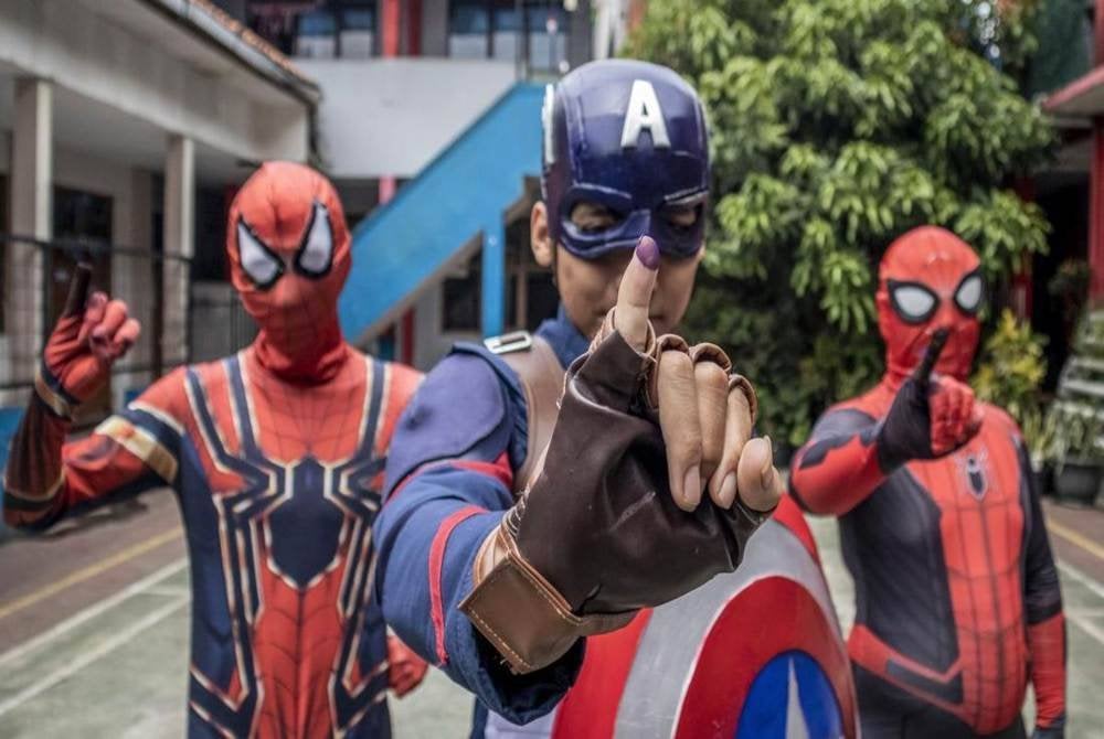 Petugas di pusat mengundi 12, Pasir Kaliki, Kota Cimahi, Jawa Barat yang mengenakan kostum adiwira menunjukkan jari kelingking mereka yang dicelup dakwat selepas mengundi.