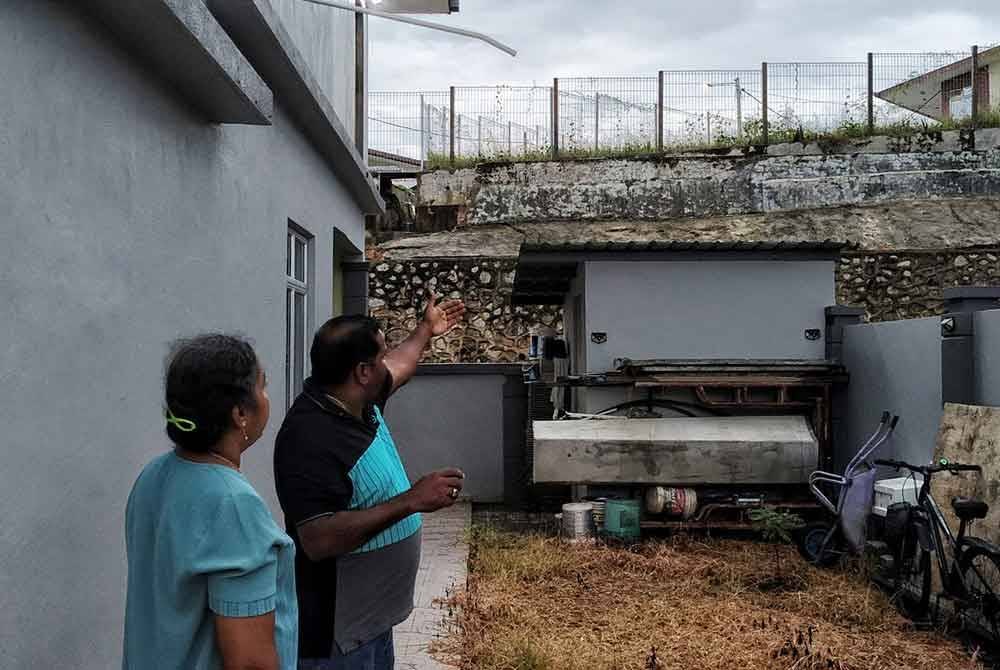 Kumaran (dua, kiri) melihat tembok yang runtuh di belakang rumahnya dalam kejadian hujan lebat pada petang Isnin.