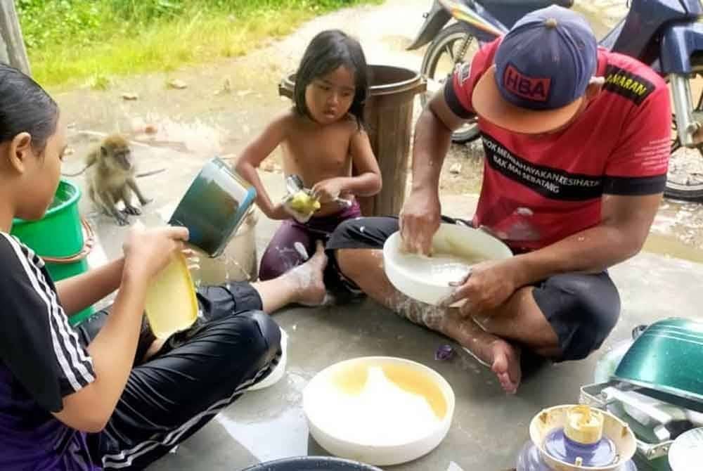 Suami serta anak-anak Faezah mencuci kelengkapan rumah yang ditenggelami banjir di Telaga Mas, Rantau Panjang.