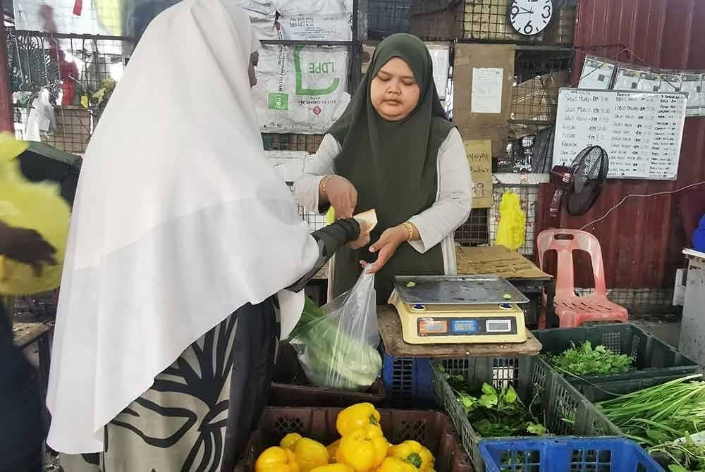 Siti Faridah melayan pelanggan yang membeli sayur di Pasar Borong Gong Pauh di Kuala Terengganu.