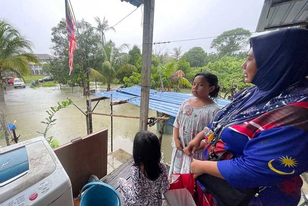 Nurul Hanim bersama dua anaknya melihat keadaan air yang naik di kawasan rumahnya.