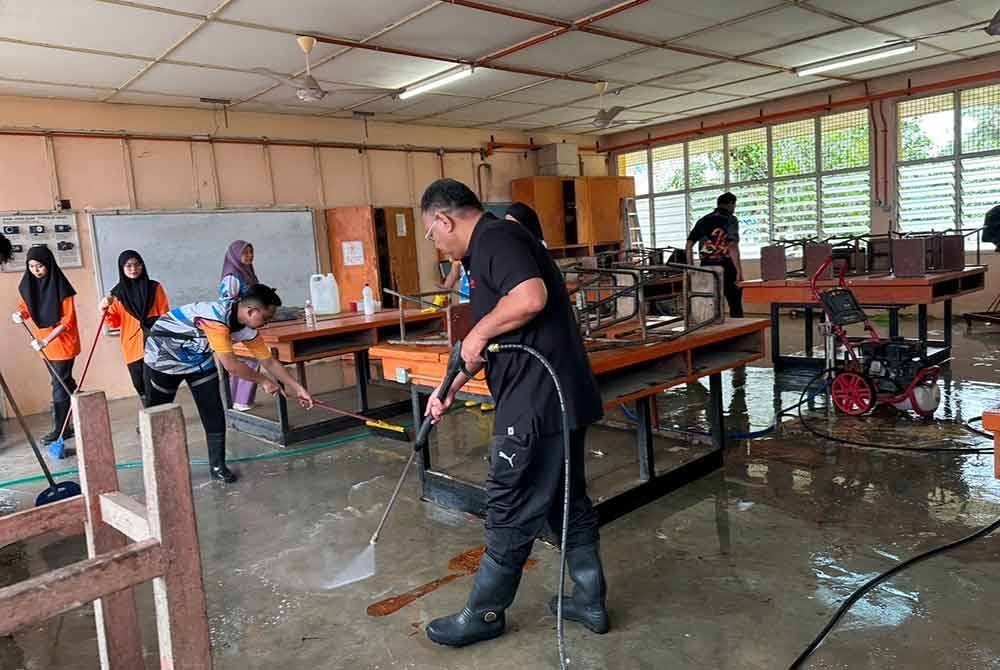 Mohd Sazili (tengah) turut membantu mencuci kesan bah di bengkel SMK Meranti di Pasir Mas. - FOTO: SINAR HARIAN/ADILA SHARINNI WAHID.