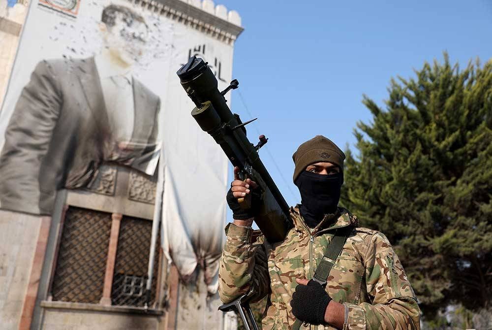 Pembebas Syria memegang senjata di hadapan bangunan yang memamparkan potret basha al-Assad yang digulingkan di bandar Hama. Syria. - AFP