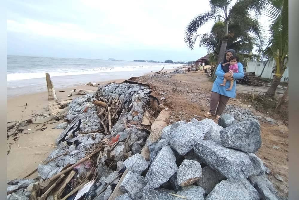 Nor Suhana menunjukkan benteng berbatu yang dibina musnah dibadai ombak ketika air pasang besar baru-baru ini.