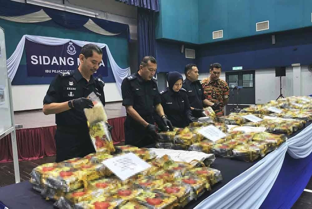 Mohd Khairi (kiri) menunjukkan antara bungkusan mengandungi dadah yang dirampas dalam operasi pada Ahad.