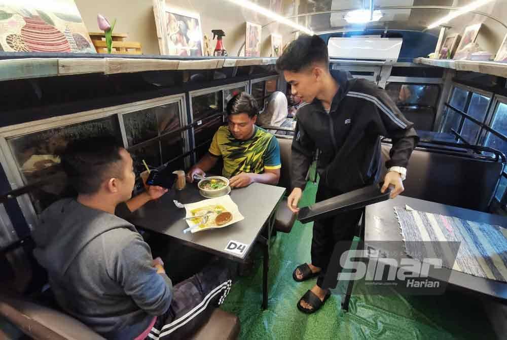 Che Mohd Ramadan (kiri) bersama Mohd Fadzil (tengah) menikmati hidangan dalam bas lama di RR Station, Kuala Berang, Hulu Terengganu.