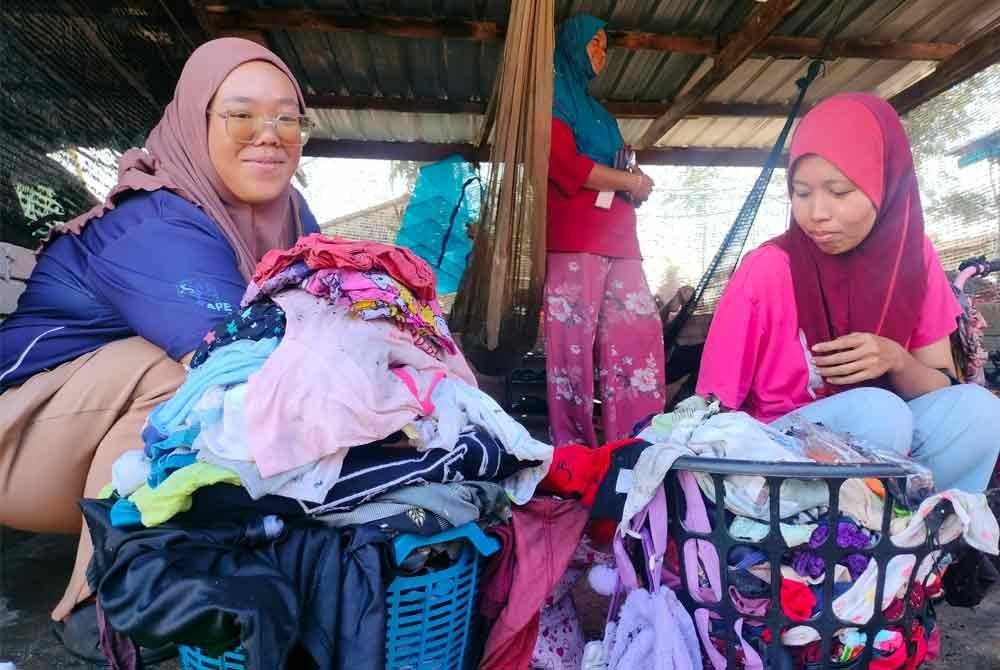 Julaili (kanan) mencari pakaian anak yang masih boleh dipakai setelah tinggal sehelai sepinggang sambil disaksikan Azlida (kiri).