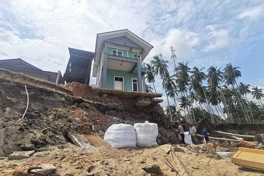 Mohd Yazit dibantu anak dan menantu membina benteng daripada guni pasir buat sementara waktu untuk menghalang rumahnya runtuh.