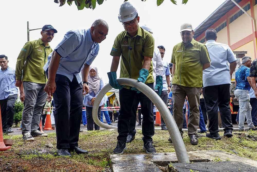 Akmal Nasrullah (tengah) mengosongkan tangki septik pada Ops Sedut IWK di Felda Ulu Penggeli sempena edisi kedua Jelajah Petra Skuad Zon Selatan pada Ahad. Foto Bernama