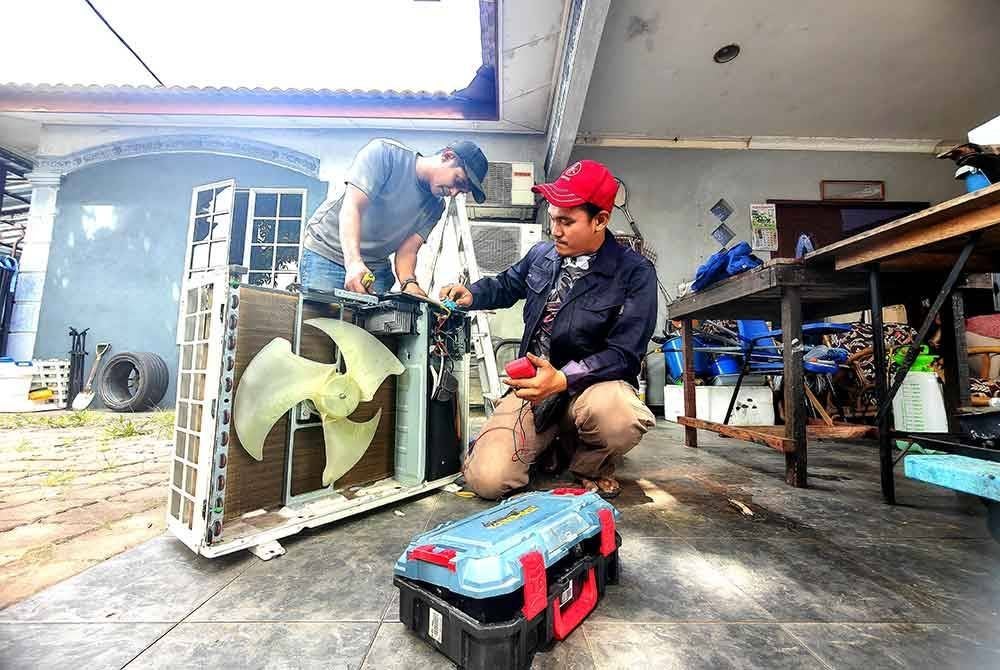 Fathir bersama rakannya melakukan kerja-kerja servis alat pendingin hawa.