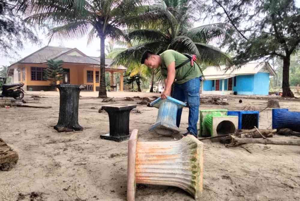 Mohd Anas membersihkan kerusi yang dilanda ombak di hadapan chalet milik keluarganya.