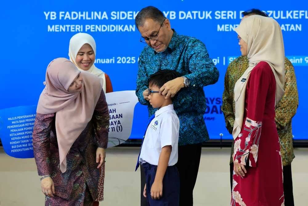 Dr Dzulkefly memakaikan kaca mata pada salah seorang murid yang menerima sumbangan sambil diperhatikan Fadhlina. Foto Bernama