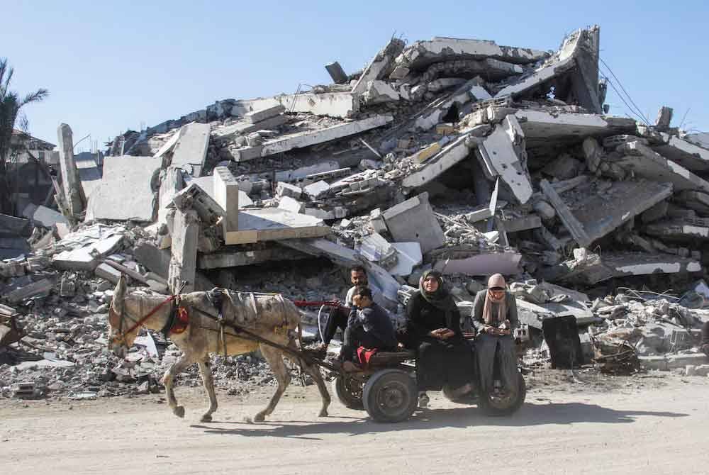 Penduduk Palestin menaiki kereta keldai melepasi runtuhan sebelum gencatan senjata antara Israel dan Hamas berkuat kuasa di Bandar Gaza pada Ahad - Foto: Reuters
